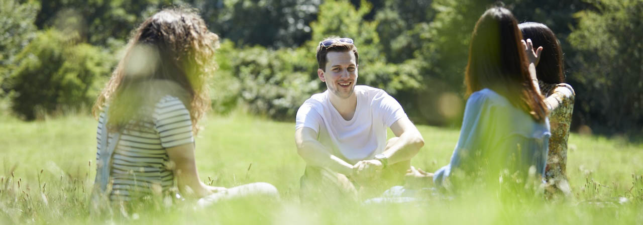 a group of postgraduate students sat in long grass with trees beyond